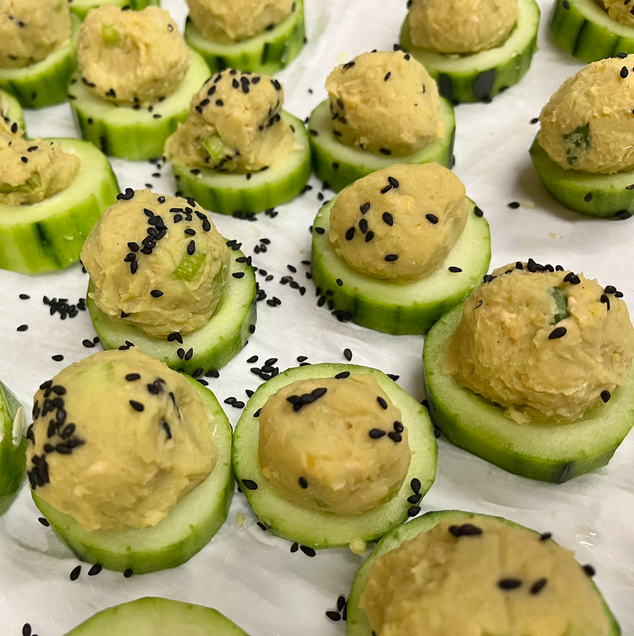 Cucumbers slices are topped with tablespoon-sized hummus balls, that are garnished with black sesame seeds.